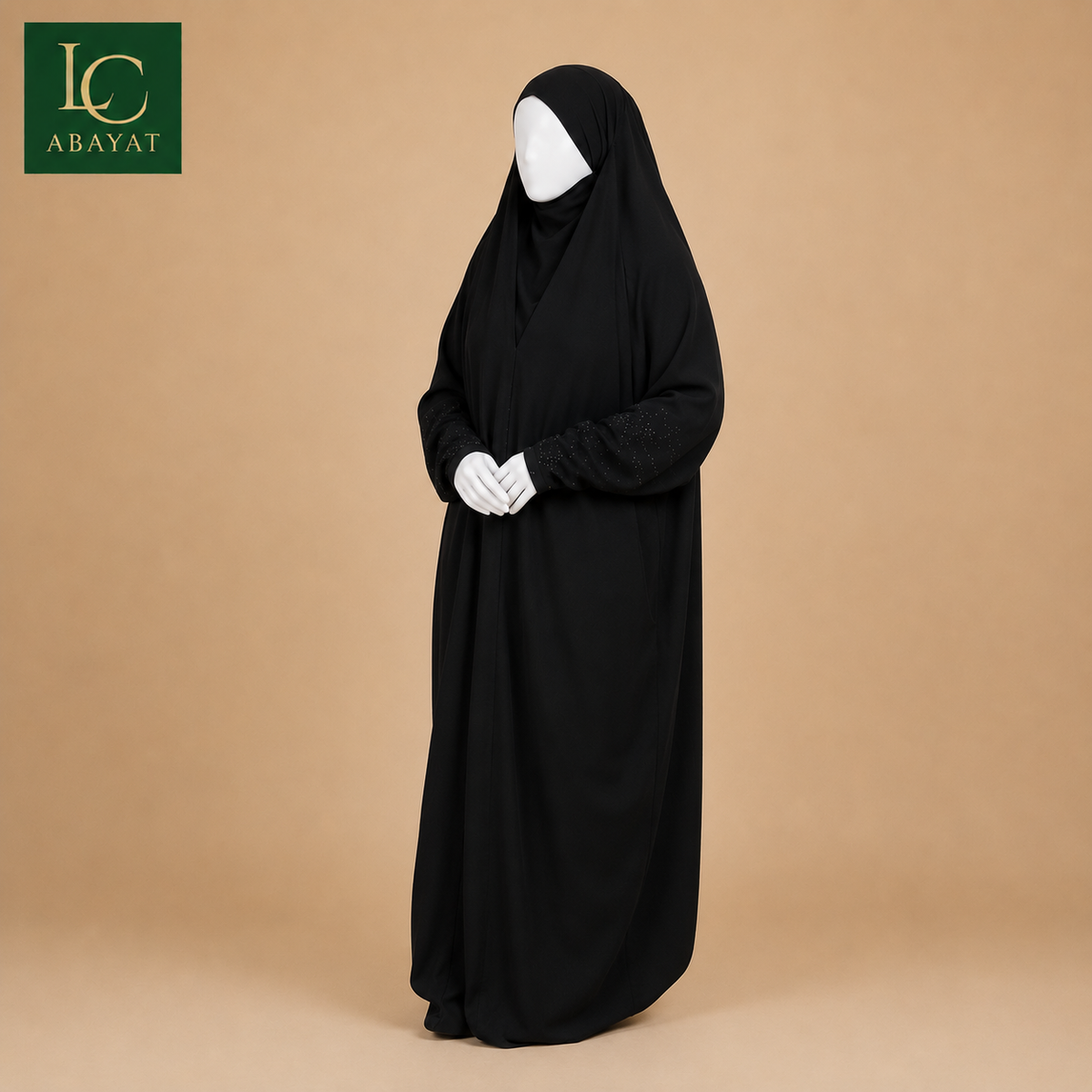 A black full-length modest garment with a hood and long sleeves, displayed on a white mannequin against a warm beige studio background. The Abayat brand logo appears in the top-left corner.