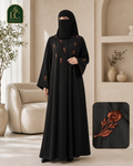A woman wearing a black full-length abaya with embroidered floral details, standing in a softly lit indoor setting. A close-up inset in the lower right shows the embroidery detail.