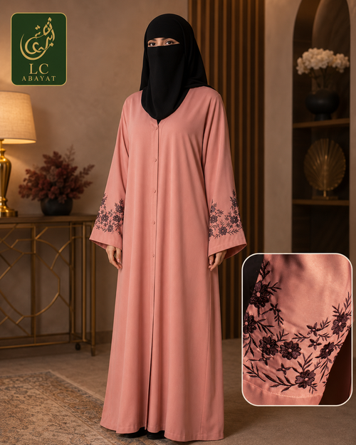 A woman wearing a long dusty pink abaya with black floral embroidery on the sleeves, paired with a black face covering, standing in an elegant indoor setting. A brand logo for 'LC ABAYAT' is visible in the top left, and a detail inset of the embroidered sleeve is shown in the bottom right.