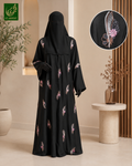 A woman wearing a black abaya and matching hijab with scattered pink feather motifs, shown in a styled indoor setting. A circular inset at the top right shows a close-up of one feather motif, and the brand logo appears in the top left corner.