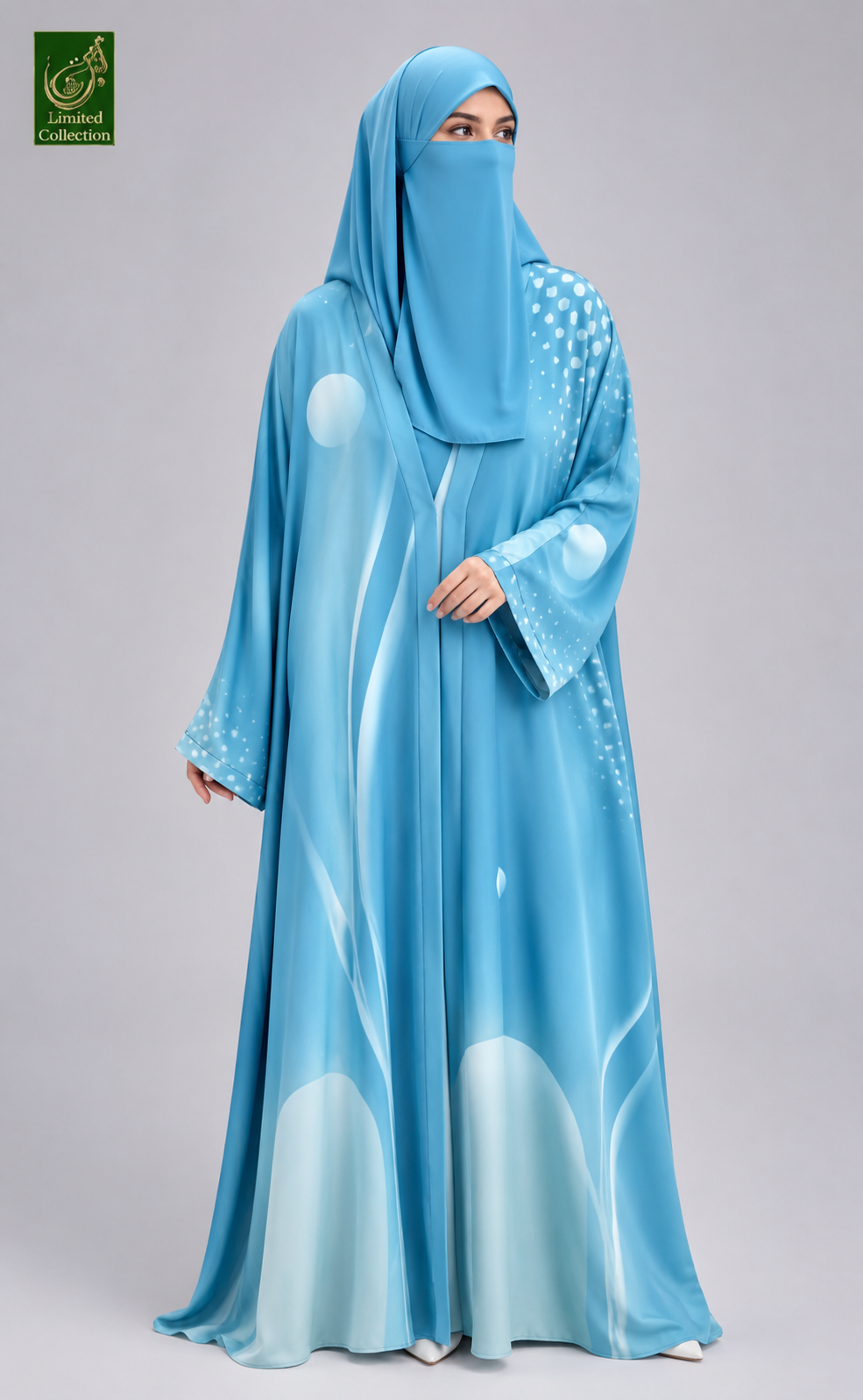 A woman wearing a light blue abaya and matching hijab with white abstract wave-like patterns, photographed against a plain light gray studio background. A green logo appears in the top-left corner.