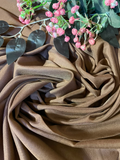 Brown draped fabric with soft folds, styled with pink flowers and dark green leaves on a matching brown background.