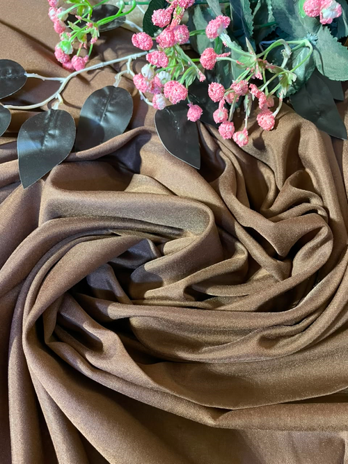 Brown draped fabric with soft folds, styled with pink flowers and dark green leaves on a matching brown background.