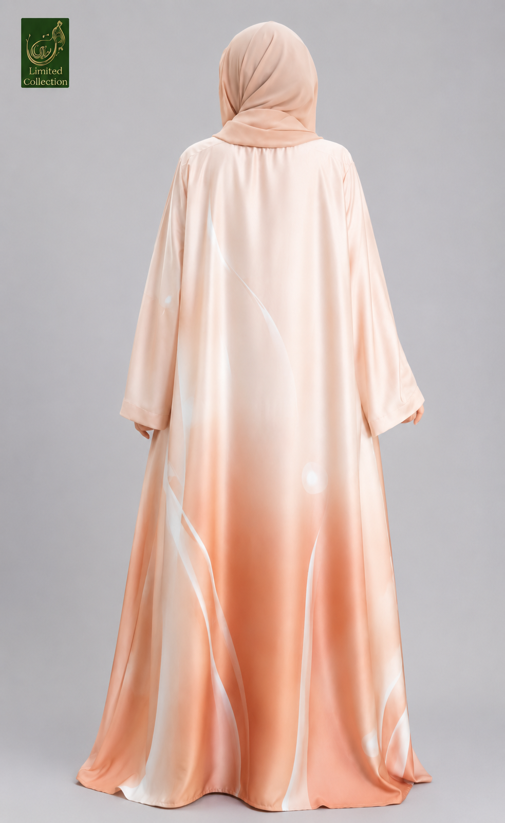 A woman wearing a flowing abaya and hijab set in a soft peach and cream gradient, shown from the back against a neutral gray studio background. A small green logo appears in the top-left corner.