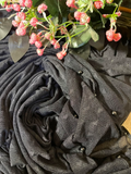 A close-up of a dark charcoal gray sheer mesh fabric draped in soft folds, decorated with small silver beads and accented by pink flowers and green leaves at the top.