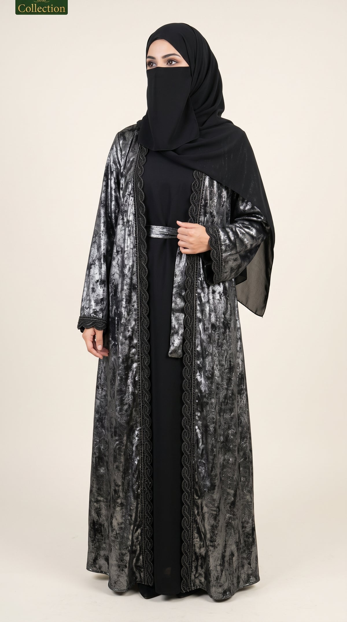 A woman modeling a black and gray patterned long abaya with a matching black hijab, standing against a plain beige studio background.