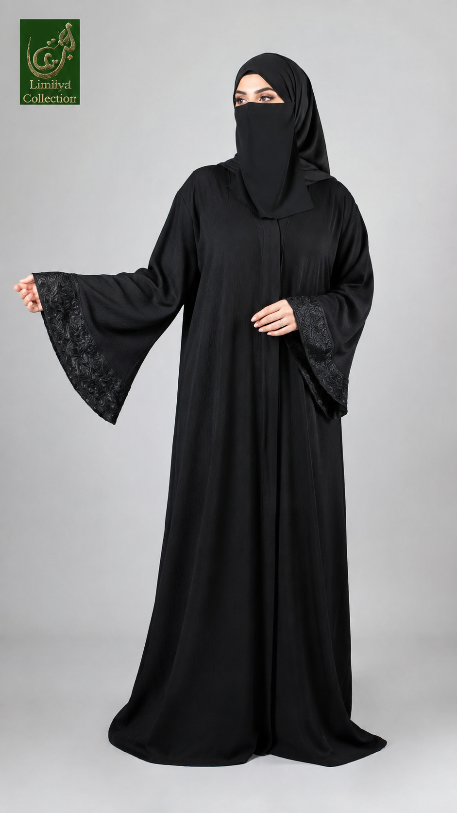 A woman modeling a black abaya with wide sleeves featuring black lace trim, paired with a matching black hijab. She is standing against a solid gray studio background, with a green 'Lindely's Collection' logo in the top-left corner.
