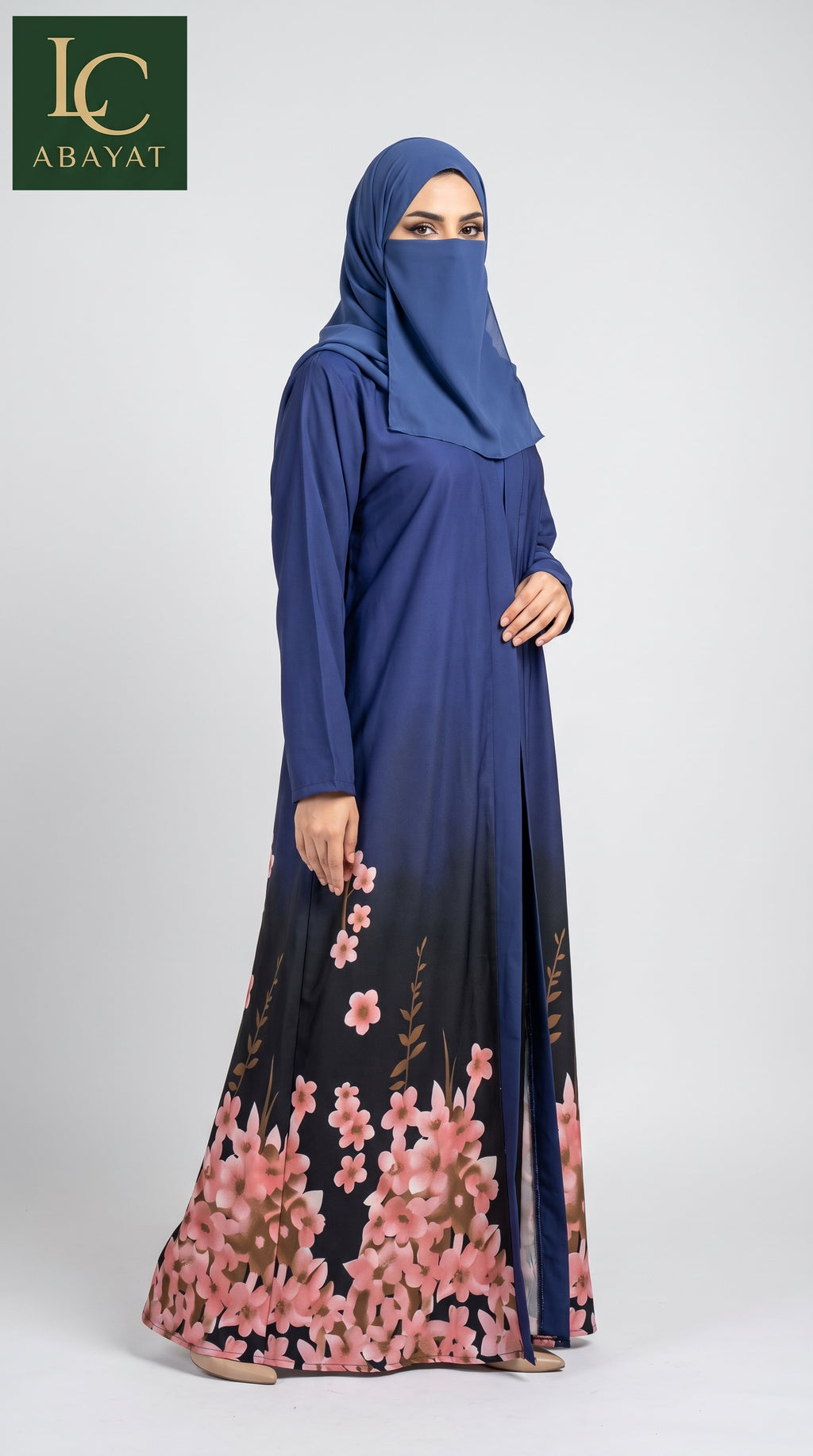 A woman wearing a navy blue abaya with a pink floral gradient print at the hem, paired with a matching navy blue hijab. The abaya features a solid navy upper body and transitions into a black base with pink and green floral patterns near the bottom.