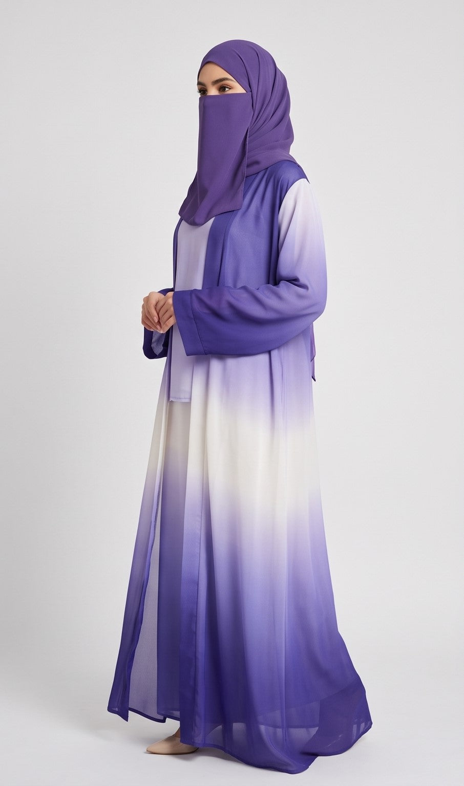 A woman wearing a blue and white ombre Kimono abaya with a matching blue hijab, standing against a light gray studio background.