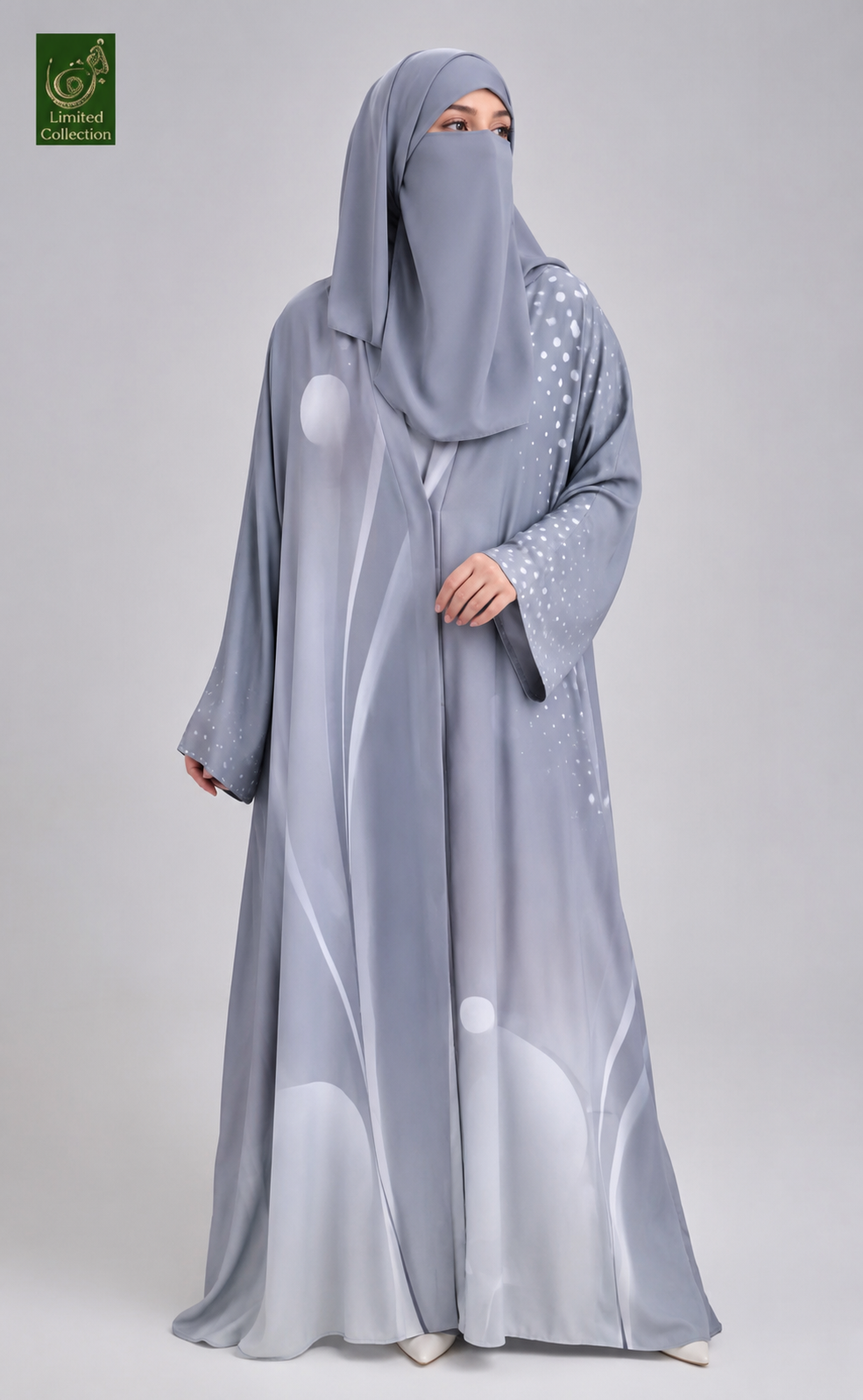 A woman wearing a light gray abaya and matching hijab with white abstract wave patterns and small silver embellishments on the sleeve, photographed against a light gray studio background.