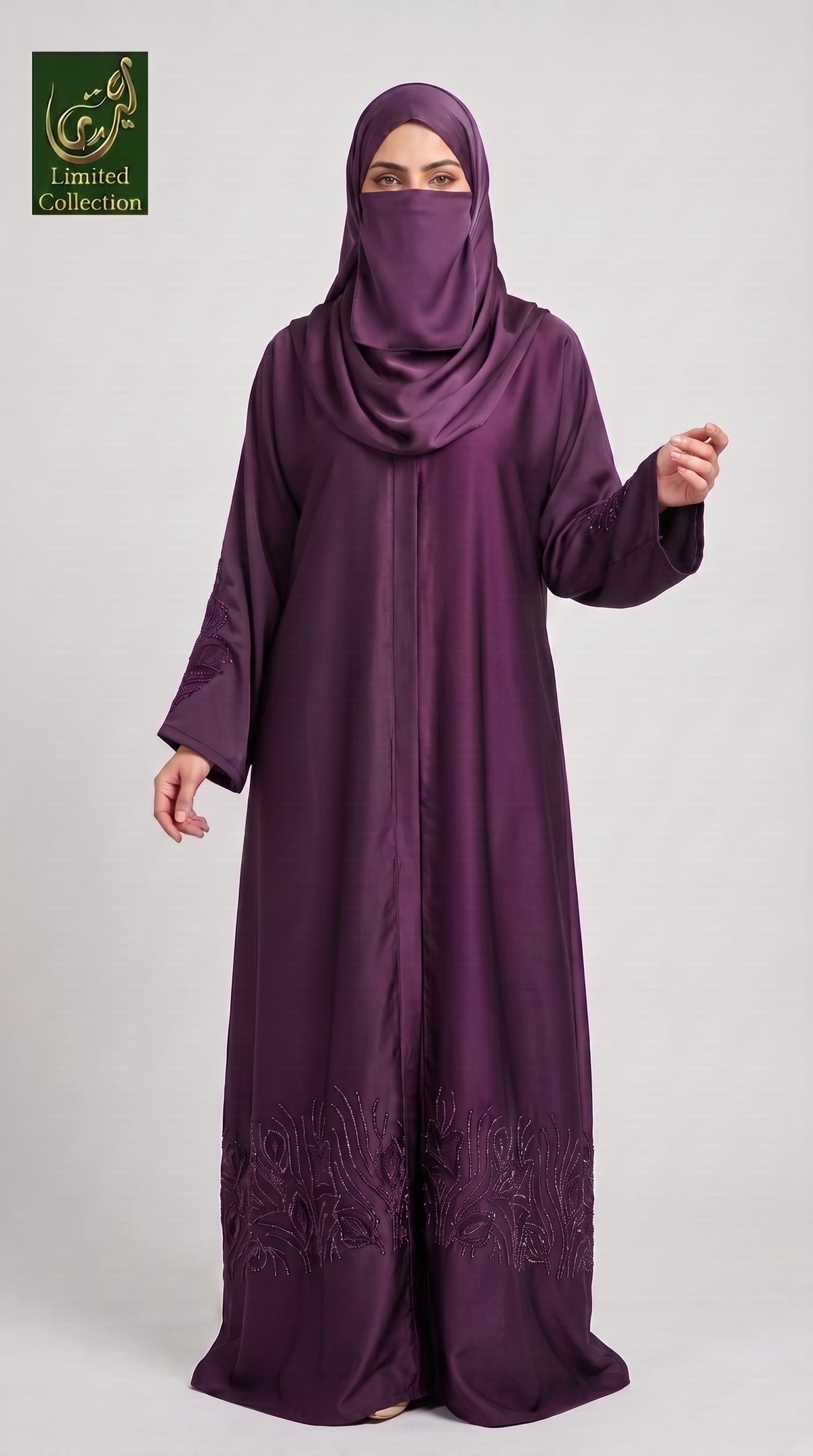 A woman wearing a long, flowing purple abaya with matching hijab and face veil, standing against a light gray studio background. The abaya has subtle embroidered detailing near the lower hem.
