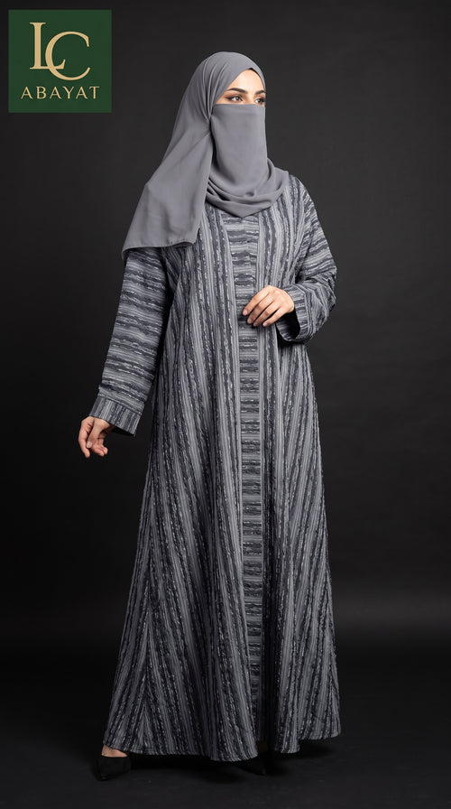 A woman modeling a long gray abaya dress with a vertical textured stripe pattern, paired with a matching gray hijab and face veil, set against a dark studio background. The 'LC ABAYAT' brand logo is visible in the top-left corner.