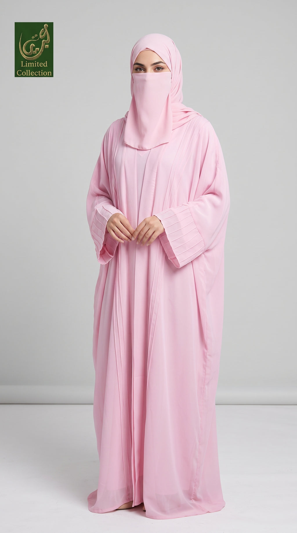 A woman wearing a light pink kimono abaya with inner and matching hijab stands against a light gray studio background. A small 'Abayat Limited Collection' logo appears in the top-left corner.