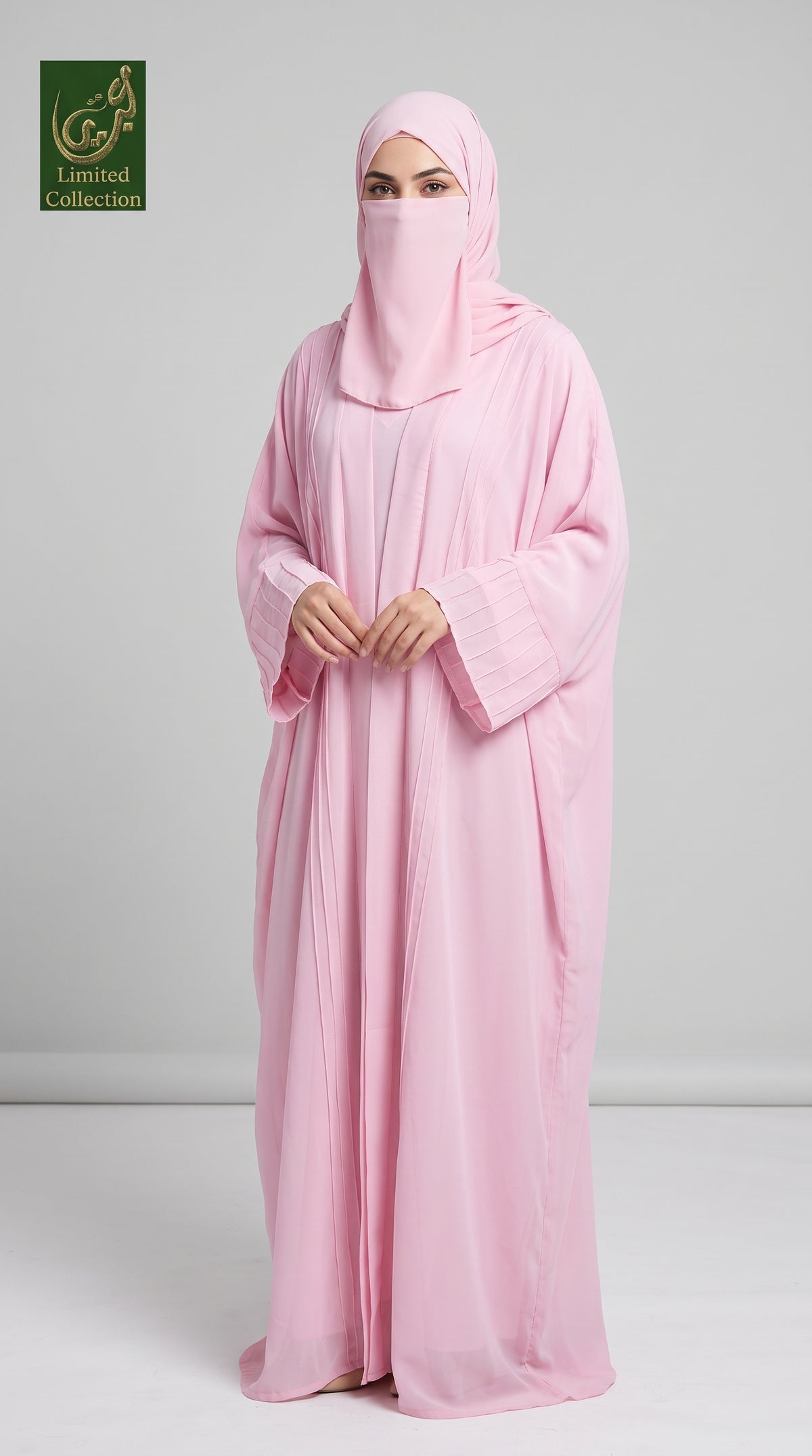 A woman wearing a light pink kimono abaya with inner and matching hijab stands against a light gray studio background. A small 'Abayat Limited Collection' logo appears in the top-left corner.