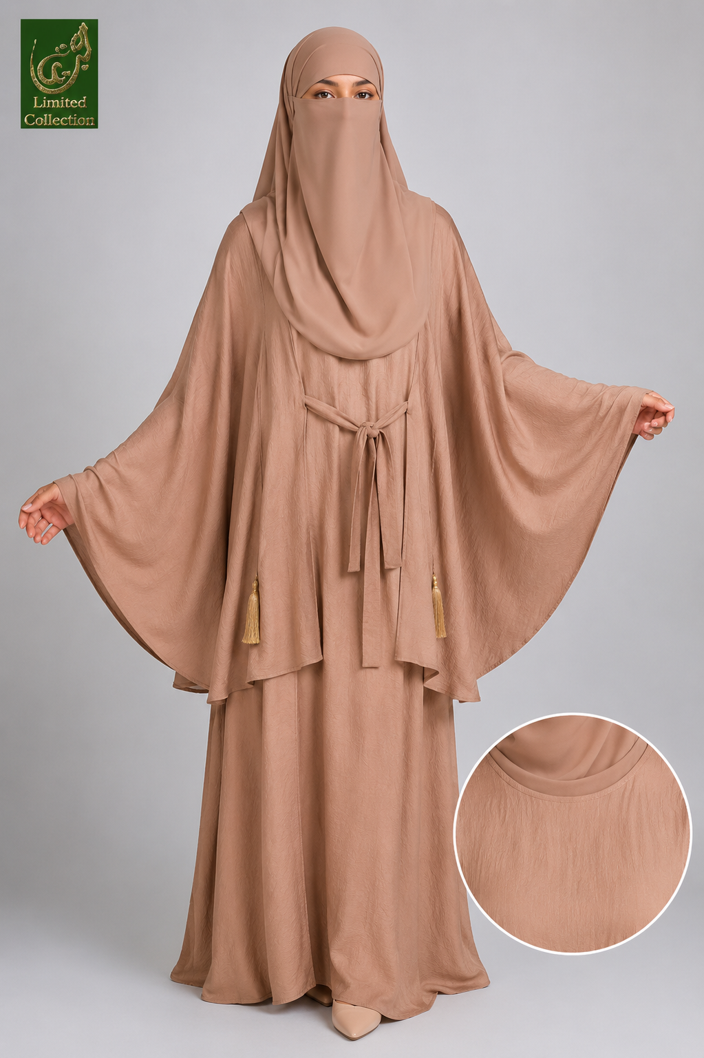 A woman modeling a modest beige abaya and matching head covering against a light gray studio background. The abaya has wide draped sleeves, a waist tie, and small tassel accents, with a circular inset showing a close-up of the fabric texture.