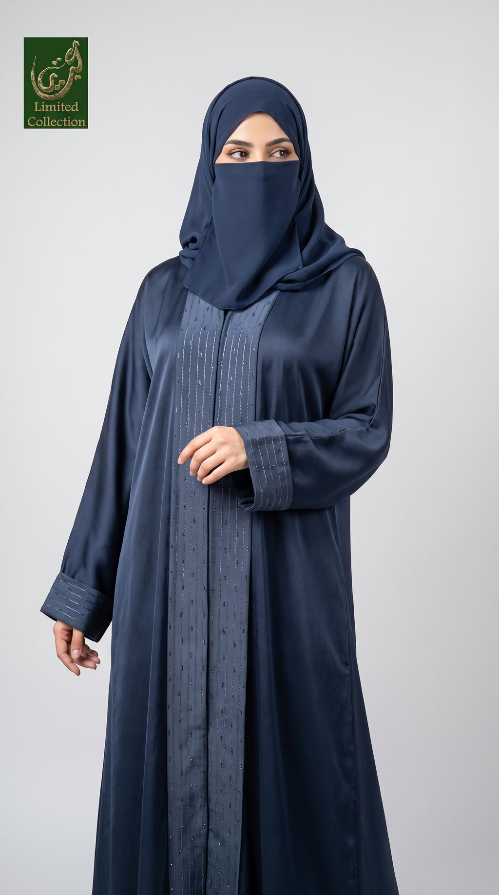 A woman wearing a dark navy blue abaya and matching hijab, standing against a light gray studio background. The abaya features a subtle textured vertical panel down the front.