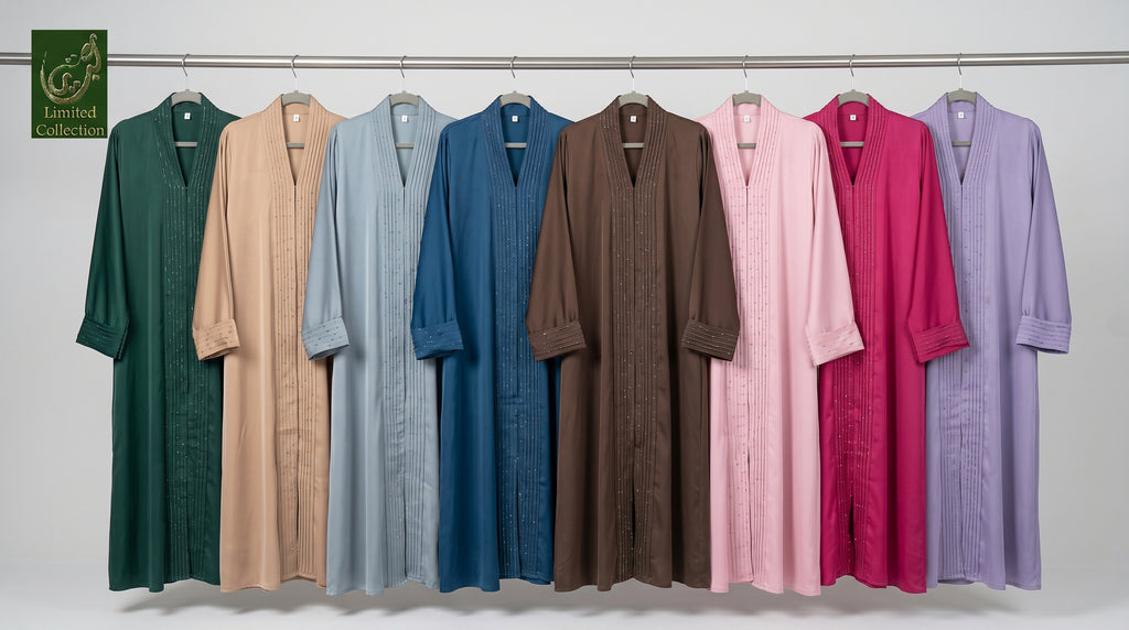 Eight long, loose-fitting ctc stonework abayas hang on a metal rod against a plain light gray wall. The robes come in multiple solid colors: dark green, beige, light blue, medium blue, brown, pink, magenta, and lavender.