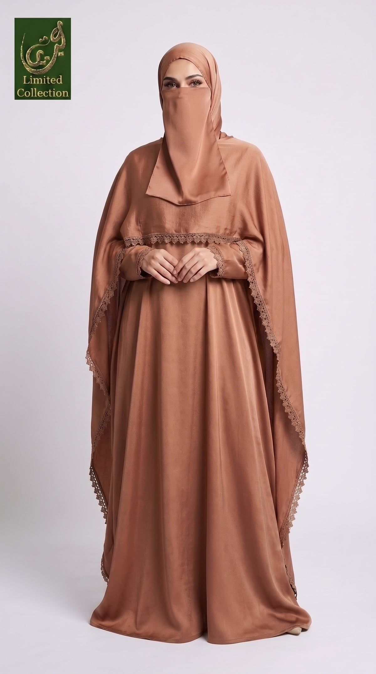 A woman wearing a flowing tan cape style maxi abaya with a matching face veil and headscarf, standing against a light gray studio background. A green 'Abayat Limited Collection' logo appears in the top-left corner.