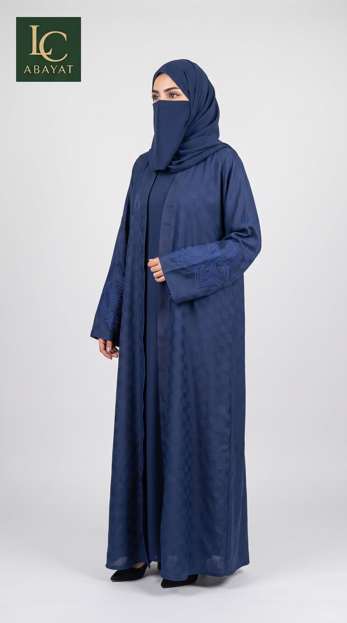 A woman wearing a navy blue abaya and matching hijab stands against a light gray studio background. The abaya has a subtle tonal pattern, and the image includes an 'LC Abayat' brand logo in the top-left corner.