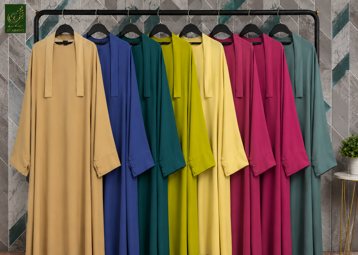 Six long Jilbabs in different colors are displayed on a black clothing rack against a gray patterned wall. The colors shown are tan, royal blue, teal, lime green, yellow, magenta, and sage green.