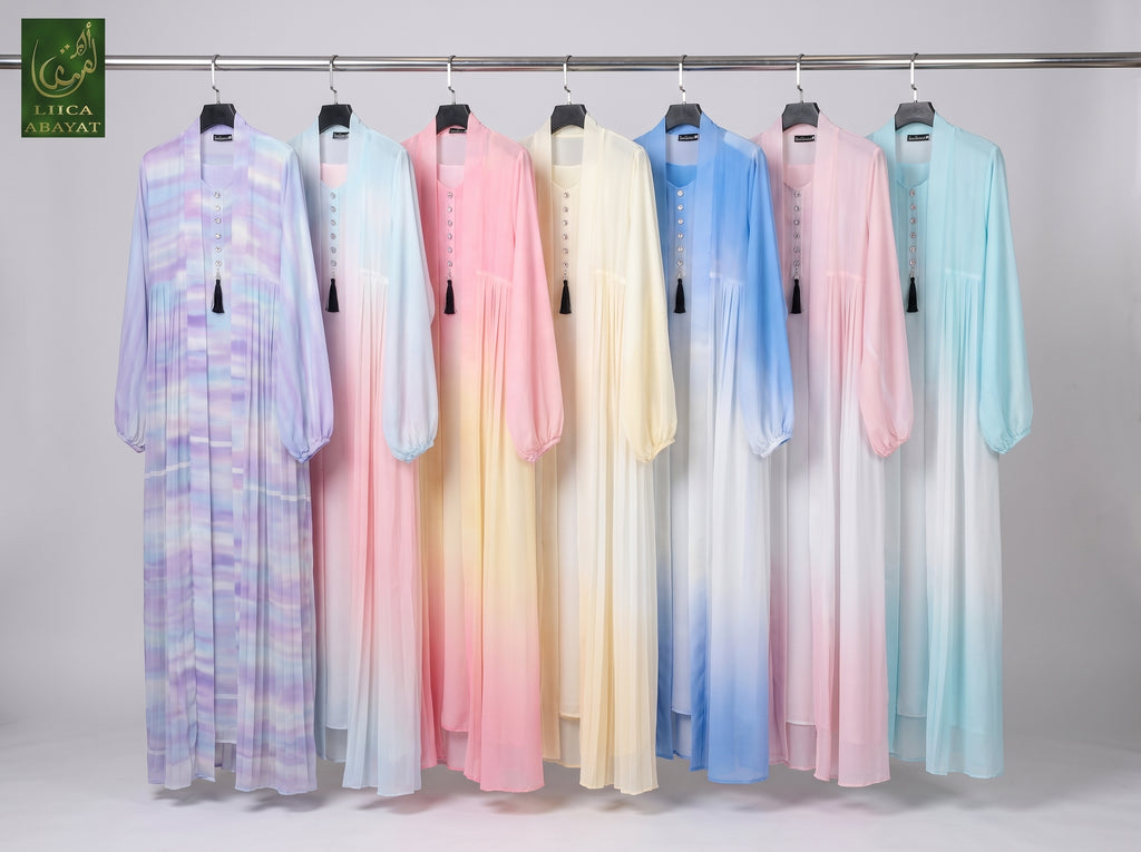 Seven long flowing Cotton Candy Tie-Dye Front-open Kimono Abaya 2pcs set hanging on a metal rack against a light gray studio background. The dresses are shown in multiple pastel colorways including lavender, pale blue, pink, cream, light blue, and mint, with soft gradient or marbled patterns.