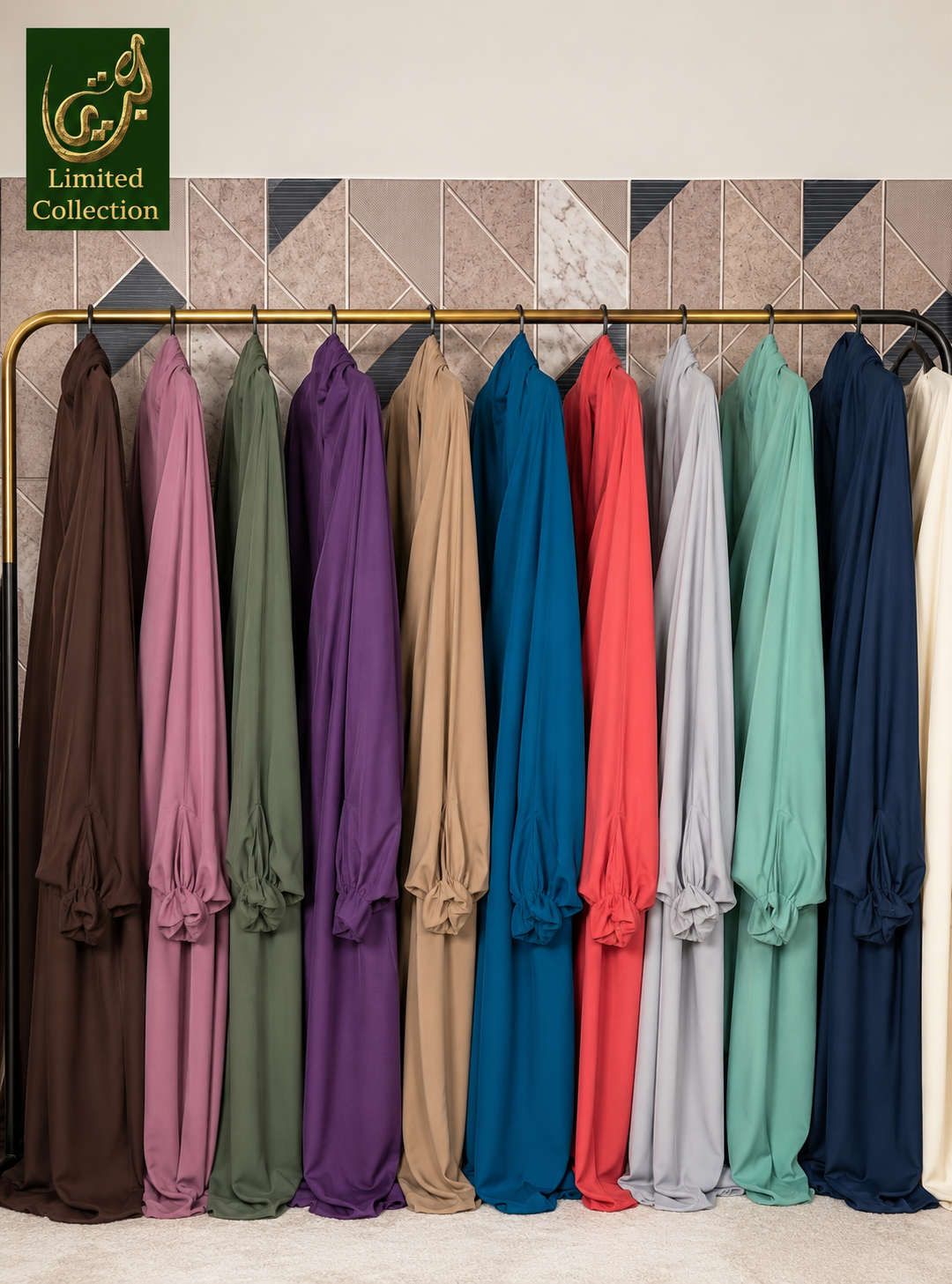 A row of long flowing jilbabs in multiple colors hanging on a rack against a patterned wall. The garments include brown, dusty pink, sage green, purple, tan, teal blue, coral red, light gray, mint green, dark navy, and cream.