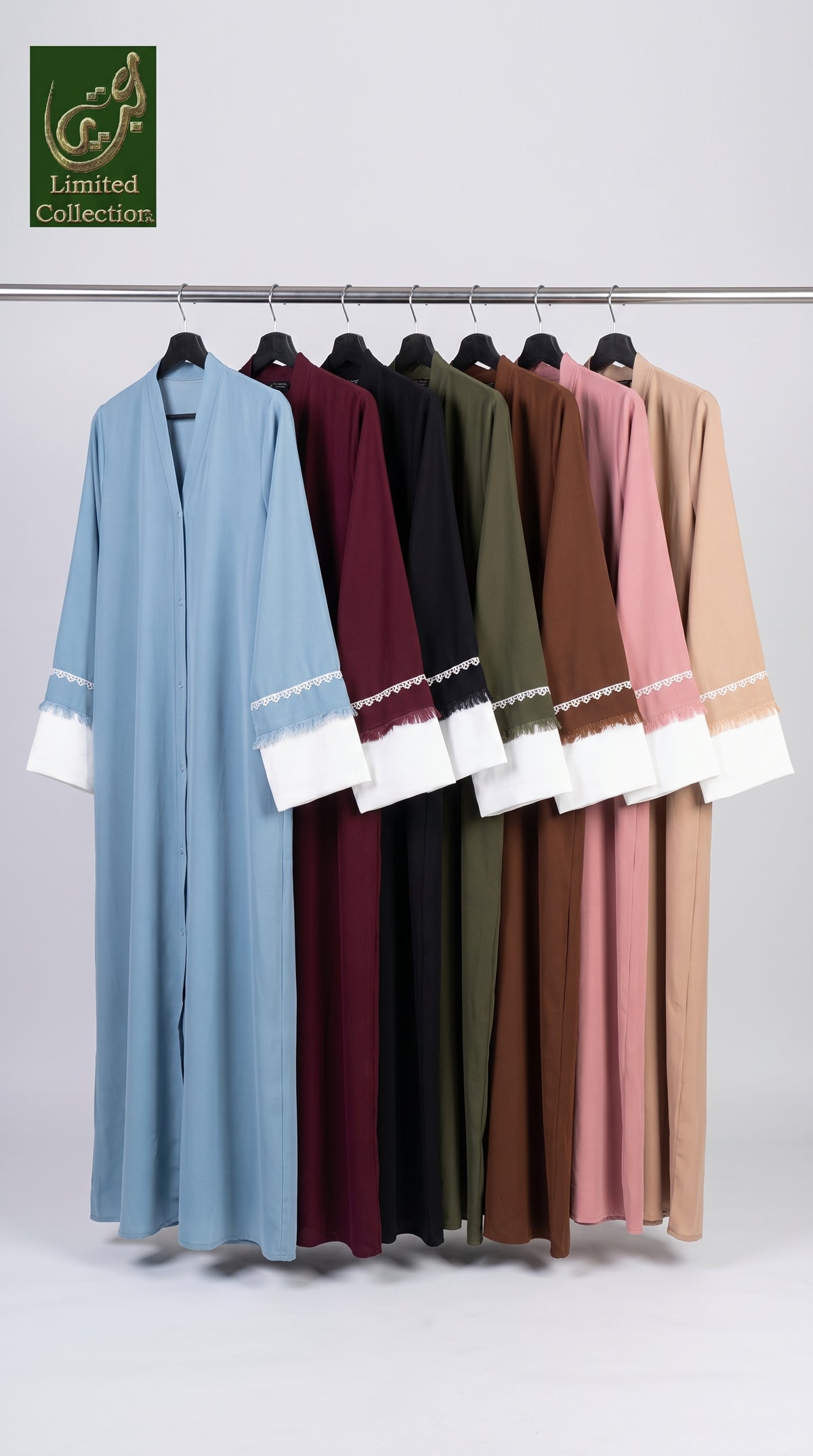 A set of long open-front abayas hanging on a metal rack against a light gray studio background. The abayas come in multiple colors including light blue, burgundy, black, olive green, brown, dusty pink, and beige, each featuring contrasting white cuffs with embroidered detailing.
