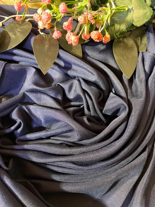 A draped piece of dark slate blue fabric with a subtle sheen, styled with artificial pink flowers and green leaves at the top.