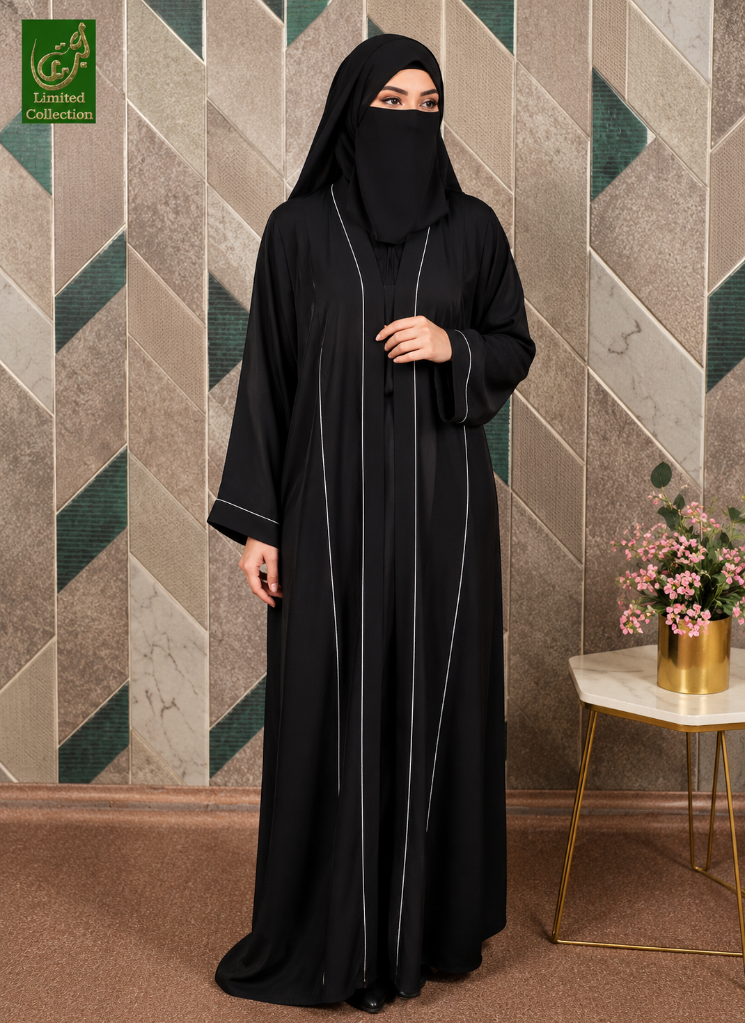 A woman wearing a black abaya and matching hijab with thin white piping details, standing in front of a geometric tiled wall. A small side table with pink flowers is visible on the right, and a green 'Limited Collection' logo appears in the top-left corner.