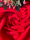 A close-up of draped bright red fabric with soft folds and a small cluster of pink flowers with dark leaves placed at the top edge.