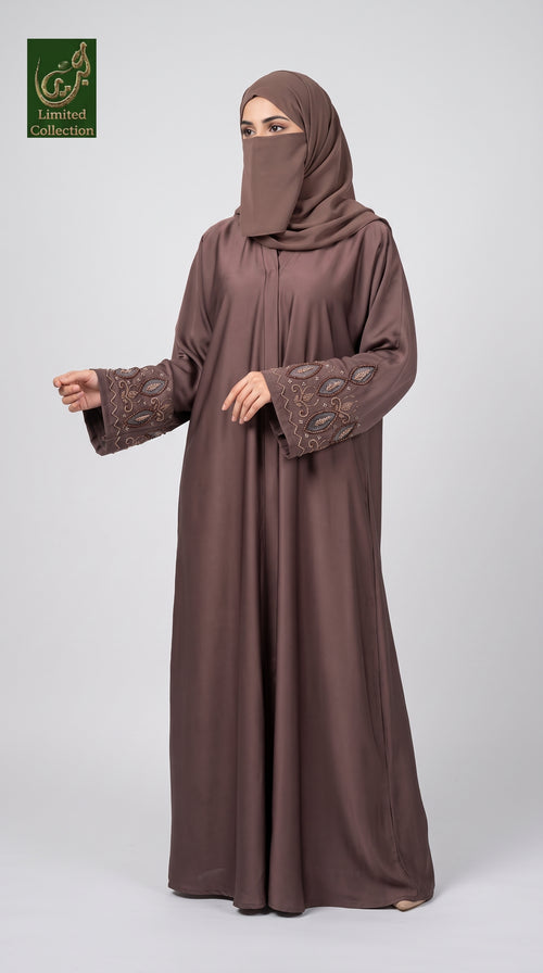 A woman modeling a long brown abaya with matching hijab, featuring embroidered detailing on the sleeves, set against a plain light gray background. A green 'GCL Limited Collection' logo is visible in the top-left corner.