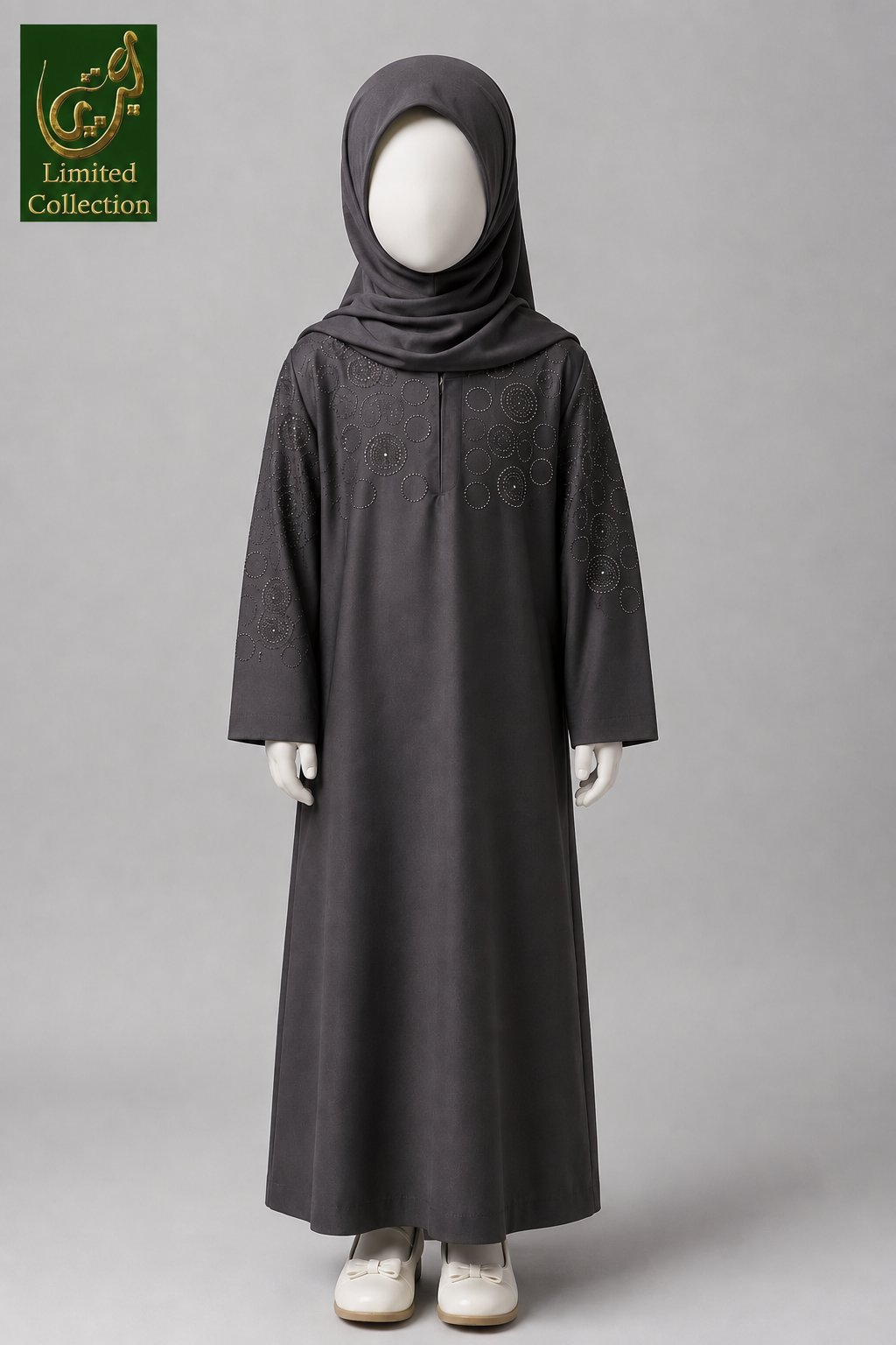 A child's long dark gray abaya dress with matching hijab, displayed on a mannequin against a light gray background. The abaya features subtle circular embroidered patterns on the chest and sleeves.