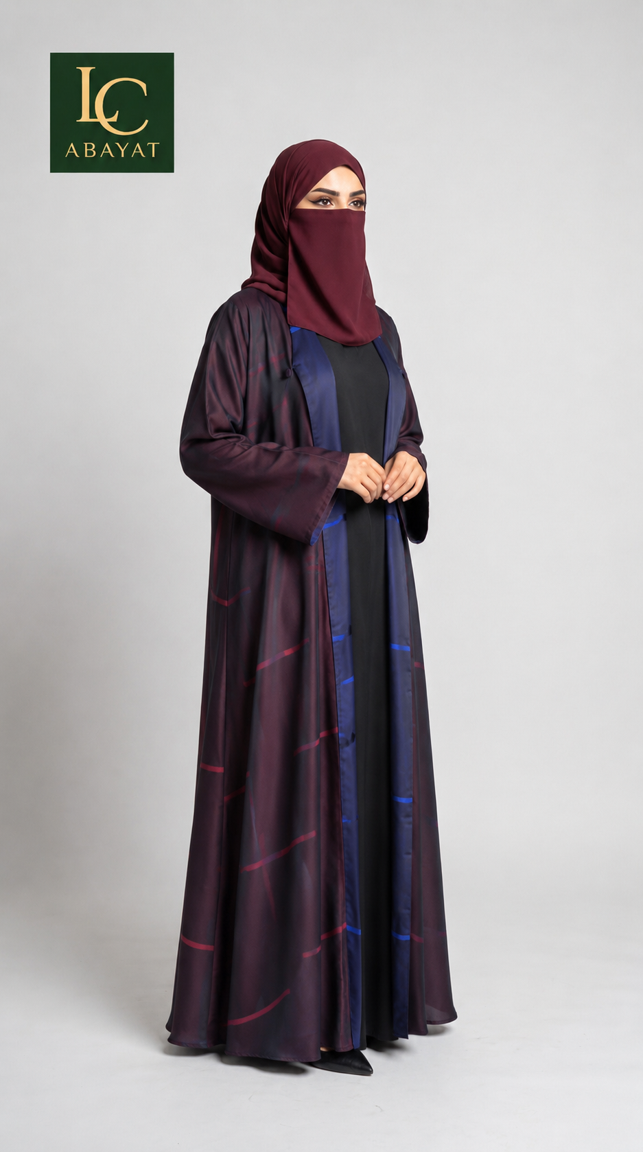 A woman modeling a long, flowing abaya with a matching hijab. The abaya is deep plum purple with a subtle sheen and thin red and blue grid-like pattern lines.