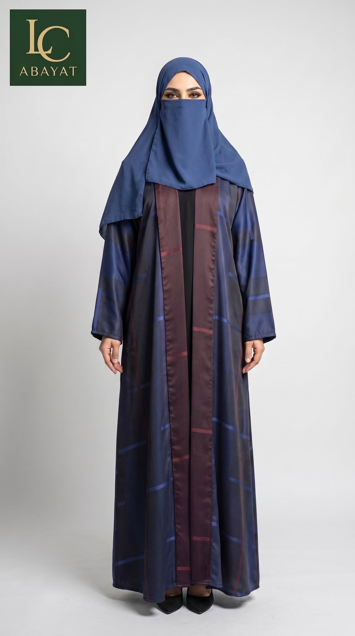 A woman modeling a long navy blue front-open reversible abaya with a subtle windowpane pattern and a matching navy blue hijab, standing against a light gray studio background. The Abayat brand logo is visible in the top left corner.