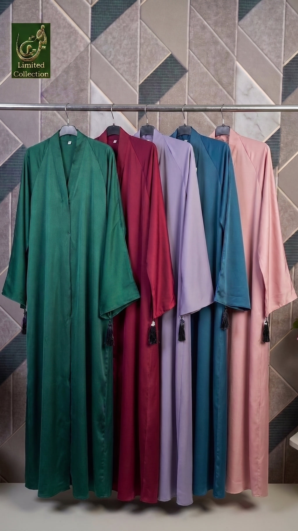 Five long flowing abayas in green, burgundy, lavender, teal, and blush pink hang on a rack against a geometric tiled wall. A Limited Collection logo appears in the top left corner.