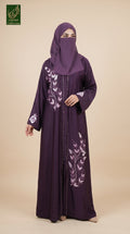 A woman wearing a long purple abaya with white floral embroidery and a matching purple hijab, standing against a solid beige background. A green 'Limited Collection' logo is visible in the top-left corner.