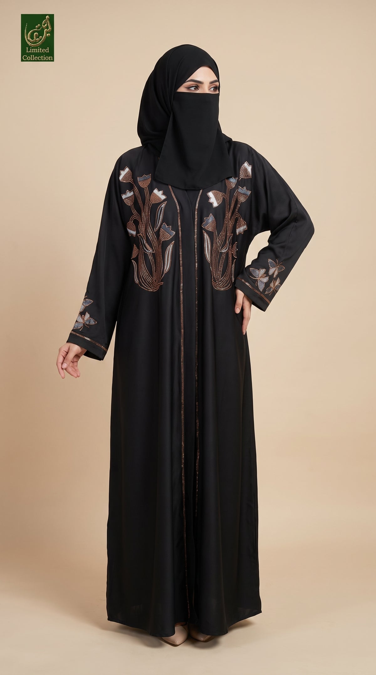 A woman modeling a long black abaya with brown and gold floral embroidery on the chest and sleeves, paired with a matching black hijab, against a solid beige background.
