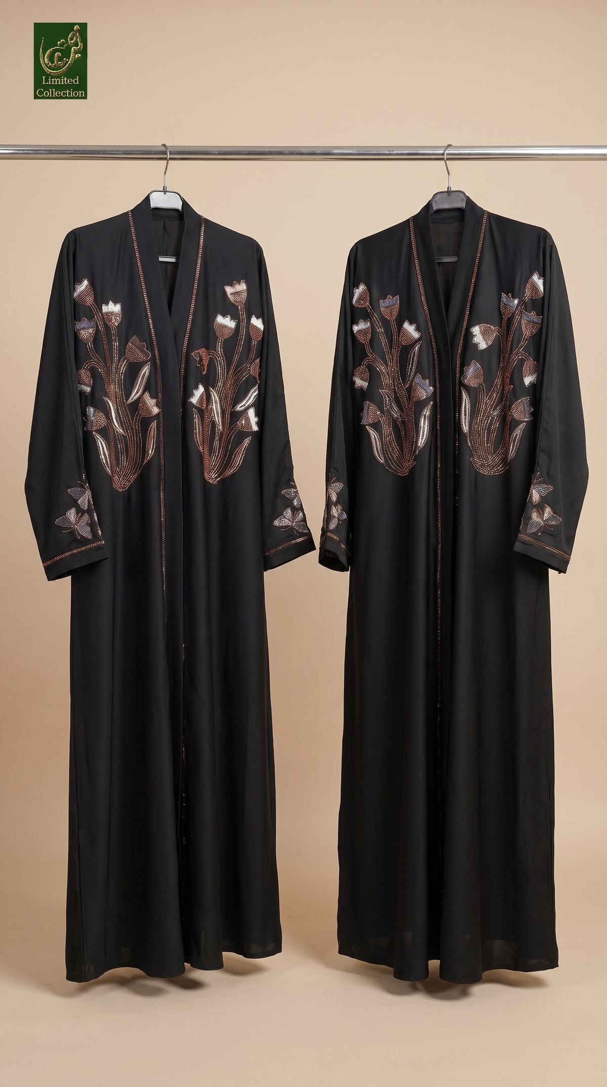Two black long open-front robes with brown and beige floral embroidery, hanging on a metal rack against a beige studio background.