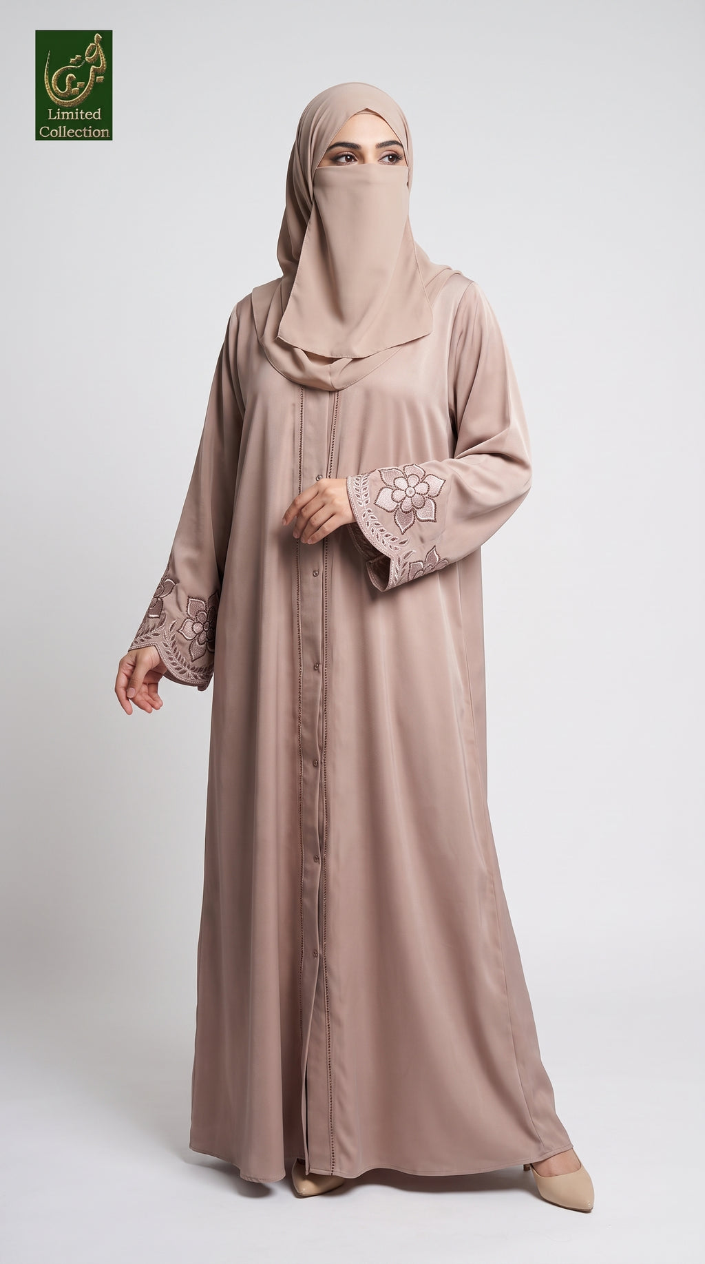 A woman modeling a long taupe-beige abaya with floral lace sleeve embroidery and a matching hijab, standing against a light gray studio background. A green 'Lumiere Collection' logo is visible in the top-left corner.
