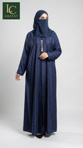 A woman wearing a navy blue abaya and matching hijab with a decorative tassel at the neckline, standing against a light gray studio background. The LC Abayat brand logo is visible in the top left corner.