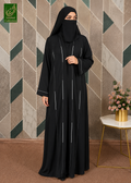 A woman wearing a black Korean Nida piping work abaya with thin vertical silver-white stripes and a matching black hijab, standing in front of a geometric patterned wall. A small side table with pink flowers is on the right, and a green 'Luxeen Collection' logo is in the top-left corner.