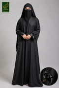 A woman wearing a long black Front-Open Dubai Style Collar Abaya with Bow-Tie Cuffs and a matching black head covering and face veil, standing against a plain gray studio background. A circular inset at the bottom right shows a close-up of a black bow detail on the garment, and a green 'Limited Collection' logo appears in the top left corner.