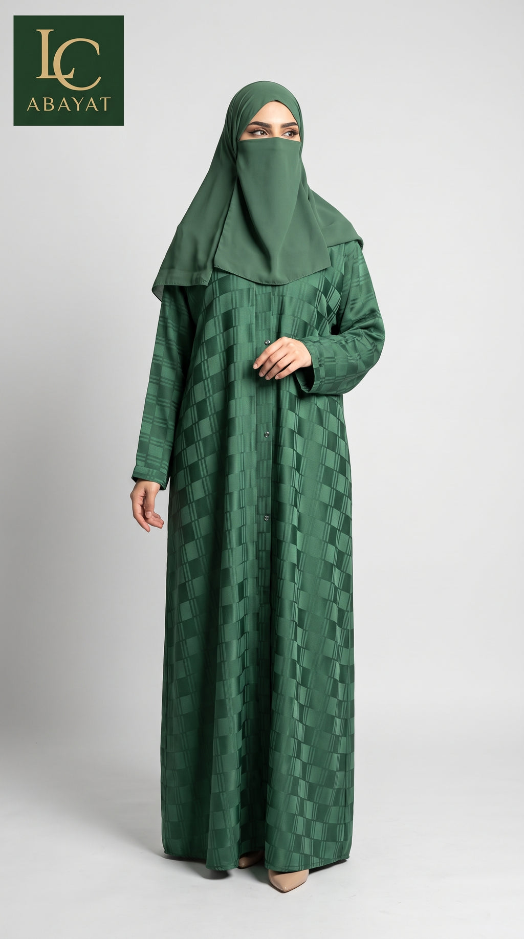 A woman wearing a long green front-open self windowpane print abaya dress with a subtle geometric pattern and a matching green hijab, standing against a light gray studio background. The LC Abayat brand logo is visible in the top left corner.