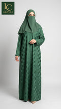 A woman wearing a long green front-open self windowpane print abaya dress with a subtle geometric pattern and a matching green hijab, standing against a light gray studio background. The LC Abayat brand logo is visible in the top left corner.