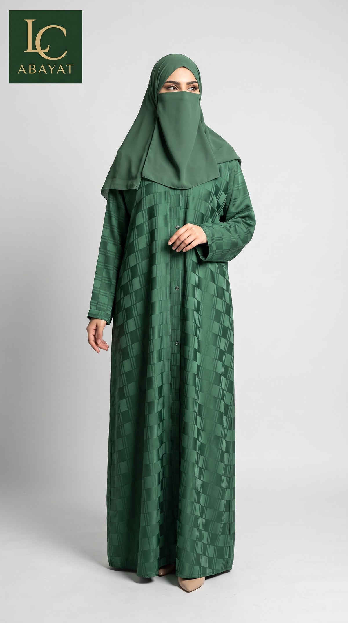 A woman wearing a long green front-open self windowpane print abaya dress with a subtle geometric pattern and a matching green hijab, standing against a light gray studio background. The LC Abayat brand logo is visible in the top left corner.