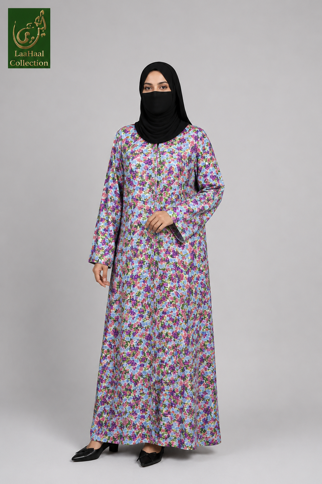 A woman modeling a long-sleeved floral front-open abaya with a black hijab and black shoes, standing against a solid gray studio background. The abaya features a dense multicolor floral print on a light lavender-purple base.