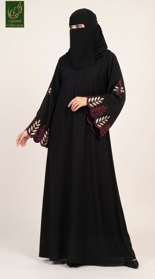 A woman wearing a black abaya with embroidered leaf patterns on the sleeves and a matching black face covering, standing against a plain light beige studio background. A green 'Limited Collection' logo is visible in the top-left corner.
