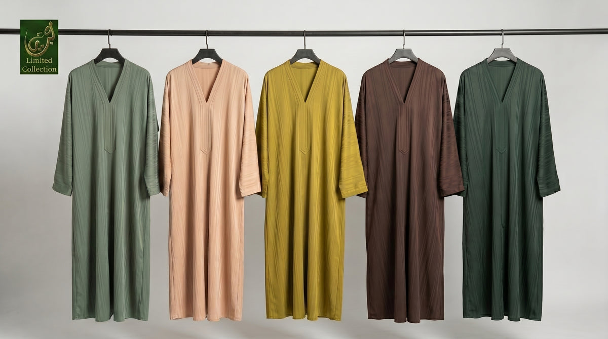 Five long, loose V-neck front-open Zoom fabric abaya hang on a black clothing rack against a light gray studio background. From left to right, the colors are sage green, blush pink, mustard yellow, dark brown, and deep forest green.