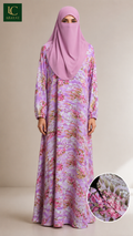 A woman wearing a long floral fron't closed maxi abaya and a matching pink hijab stands against a plain beige studio background. The dress has a pink, purple, and white floral pattern.