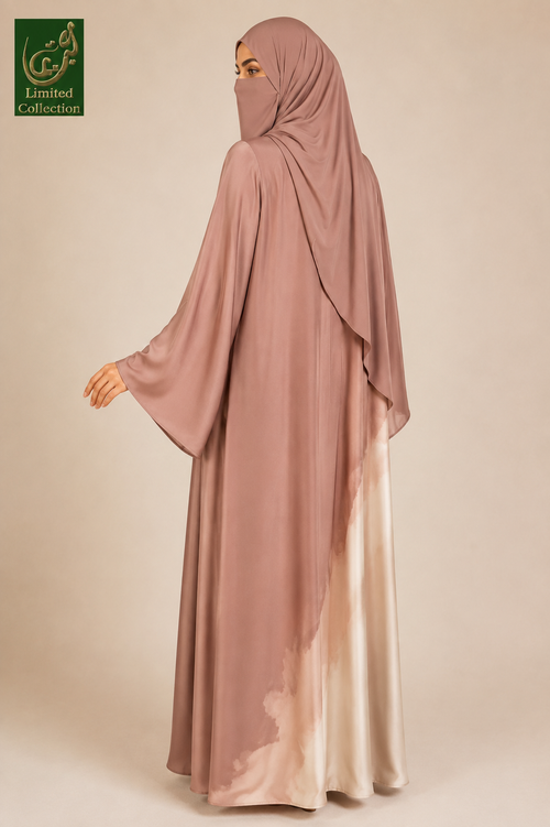 A woman wearing a modest long abaya and matching hijab in a dusty rose color with a satin-like lower hem that fades into a light champagne tone, shown against a plain beige studio background. A green 'Limited Collection' logo appears in the top-left corner.